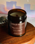 Candle jar labeled 'Gold Rush' on a wooden stand with disco balls in the background