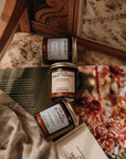 Three small jars with labels on a textured surface with floral patterns in the background