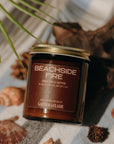 Candle labeled 'Beachside Fire' by Gather of Flame on a surface with natural elements like shells and wood.