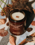 Candle labeled 'Beachside Fire' on a striped fabric with seashells and driftwood.