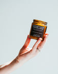 Hand holding a 'Champagne Problems' candle jar against a light background