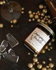A jar candle with a label reading 'Champagne Problems' surrounded by broken glass and gold metallic balls