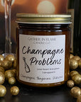 A jar candle with a label reading 'Champagne Problems' surrounded by gold metallic balls