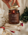 Candle jar labeled 'City of Roses' being held by a hand with decorative elements around it.