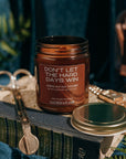 Candle jar with text 'Don't let the hard days win' on a decorative surface with books and scissors.