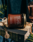 Jar of 'Don't Let the Hard Days Vanish' candle on a book with decorative elements