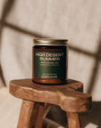 Candle labeled 'High Desert Summer' on a wooden stool with soft lighting