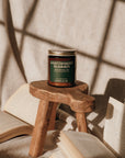 Candle on a wooden stool with open books and a textured wall background