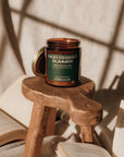 Candle labeled 'High Desert Summer' on a wooden stool with books in the background