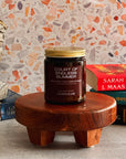 Candle on a wooden stand with books and a decorative wall in the background