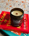 Candle in a 'Court of Thorns and Roses' book-themed container on top of books with a colorful background.