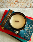 Candle in a holder on top of 'A Game of Thrones' books with a textured wall background