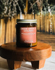 Jar of 'Once Upon a Churro' candle on a wooden stand with a blurred natural background