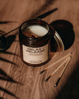Candle labeled 'Relax + Release' on a wooden surface with shadows cast by leaves.