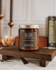 Candle jar labeled 'Slow Burn' on a wooden stand with books and candles in the background.