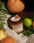 Sugared Citrus candle surrounded by fruits and leaves on a textured surface