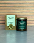 Candle labeled 'All Too Well' with packaging on a wooden surface