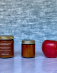 Two candles labeled Cardigan and a red apple on a textured surface with a gray background