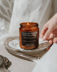Candle labeled 'Champagne Problems' on a decorative tray with a hand reaching towards it.