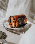 Candle jar labeled 'Champagne Problems' on a white surface with a blurred background
