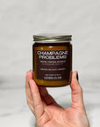 Candle jar labeled 'Champagne Problems' held by a hand against a light gray background