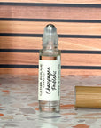 A perfume oil roller with a clear glass body and bamboo cap sitting beside it, labeled 'Champagne Problems', resting on a terrazzo surface with wood background.