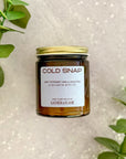 Candle jar labeled 'Cold Snap' with a gold lid on a white background with green leaves.