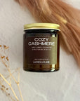 Jar of 'Cozy Cashmere' candle with gold lid on a soft background with dried pampas grass and baby's breath