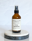 A brown amber spray bottle labeled 'Cozy Cashmere' on a white marble surface.