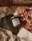 Jar of 'Cruel Summer' candle on a floral-patterned surface with a book and fabric.