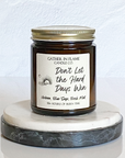 A coconut wax candle jar with a label that reads 'Don't Let the Hard Days Win', placed on a marble surface, with a white background and a gold lid on top.