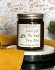 Amber jar candle labeled Don't Let the Hard Days Win on a black surface with terrazzo background, eucalyptus, and a yellow towel.