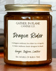 Close up of a jar candle labeled 'Dragon Rider' from Gather in Flame Candle Co.,' placed on a wooden pedestal, with books and a window in the background.