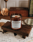 Candle labeled 'Enemies to Lovers' on a wooden stand with stationery items in the background.