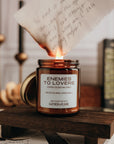 Note being lit with a candle, surrounded by books and candles on a wooden stand.