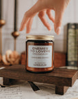 Candle labeled 'Enemies to Lovers' on a wooden stand with a hand reaching towards it.