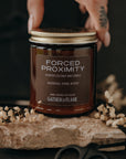 Jar of 'Forced Proximity' candle by Gather and Flame on a dark background with dried flowers and scissors.