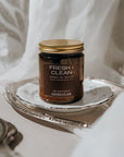 Jar of 'Fresh + Clean' candle on a silver tray with a white fabric background