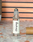 A perfume oil roller with a clear glass bottle and a bamboo cap sitting beside it, labeled 'Glamping', resting on a terrazzo surface with wood background.