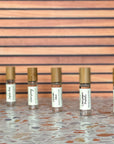 Six perfume oil rollers with clear glass bottle and bamboo cap sin a diagonal line, resting on a terrazzo surface with wood background.