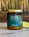 Candle jar labeled 'Glass Garden' by Gather in Flame on a marble surface with blurred background