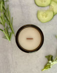 Candle in a glass jar topdown view with cucumber slices and rosemary on a light surface