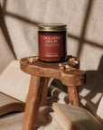 Candle labeled 'Golden Hour' on a small wooden stool with books and a textured wall in the background