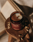 Candle in a decorative jar on a wooden stand with a neutral background