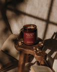 Candle labeled 'Golden Hour' on a small wooden stool with books and fabric in the background
