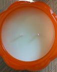 Orange pumpkin candle showing the candle surface with two wicks on a textured surface