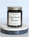 A jar candle with a label reading 'High Desert Summer', placed on a marble surface.