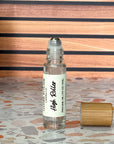 A clear perfume oil roller with a bamboo cap sitting beside it, labeled 'High Roller' on a terrazzo surface with wood background.