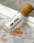 A clear perfume oil roller with a bamboo cap labeled 'High Roller' on a terrazzo surface.