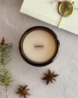 Topdown view of candle with wood wick surrounded by star anise, pine needles and a handwritten letter with wax seal on a textured surface